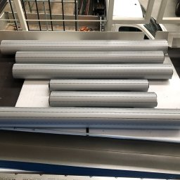 DOOR Filipek sp.k Producent ślusarki i stolarki budowlanej z aluminium i PCV - Przygotowane do montażu aluminiowe profile rolet zewnętrznych w warsztacie, widoczny karton, elementy konstrukcji stalowej i częściowo biały samochód dostawczy w tle.