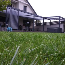 DOOR Filipek sp.k Producent ślusarki i stolarki budowlanej z aluminium i PCV - Nowoczesna pergola z regulowanymi lamelami przy domu jednorodzinnym, widok z poziomu trawnika, w tle zestaw mebli ogrodowych i jacuzzi.