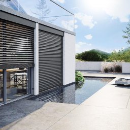 DOOR Filipek sp.k Producent ślusarki i stolarki budowlanej z aluminium i PCV - Nowoczesny dom z szarymi roletami na oknach i tarasem z basenem, widok na góry w tle.