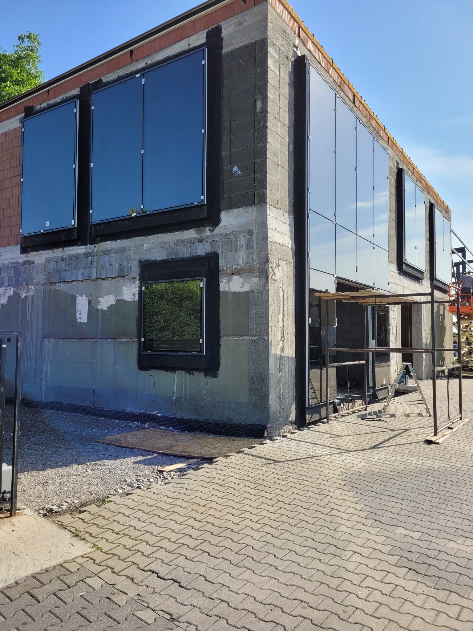 Montaż okien PCV w surowym budynku, widoczne okna z czarnymi ramami, ślady po tynku i rusztowanie w tle.