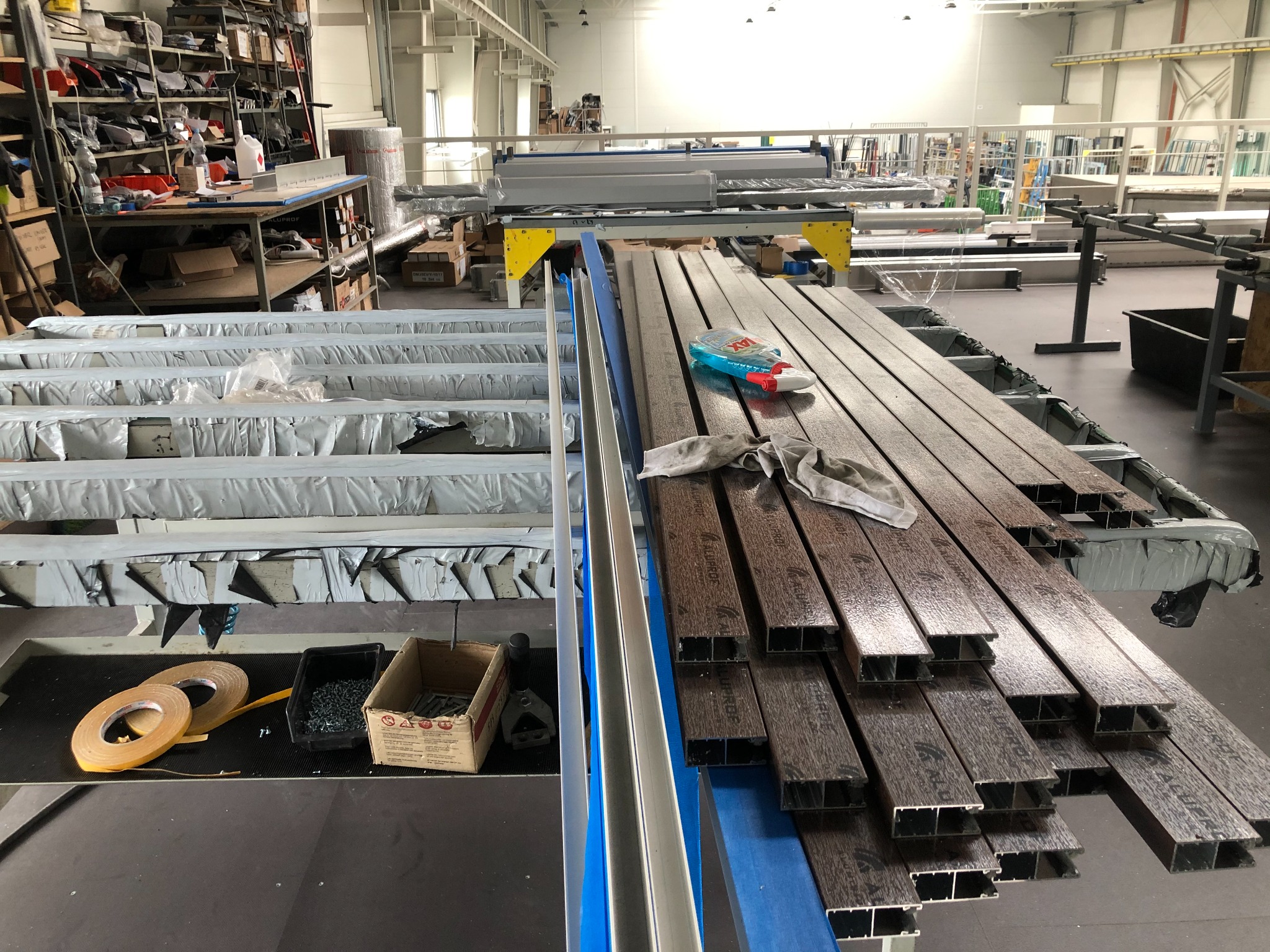 Produkcja profili aluminiowych o strukturze drewna w hali: detale cięcia, przygotowane elementy, narzędzia i akcesoria na stanowisku pracy.