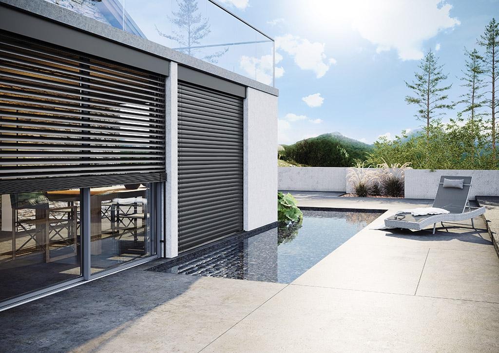 Nowoczesny dom z szarymi roletami na oknach i tarasem z basenem, widok na góry w tle.