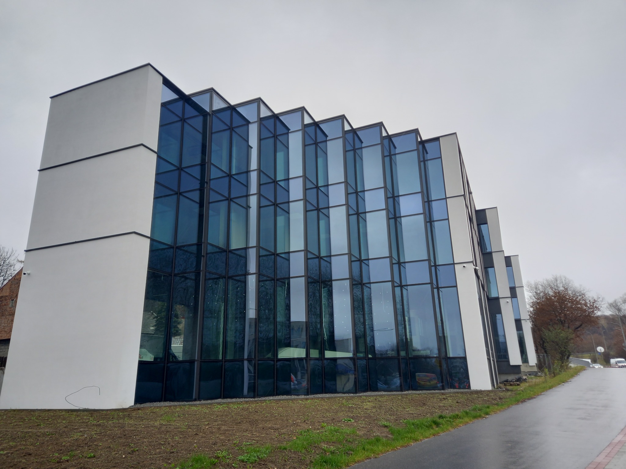 Nowoczesny budynek biurowy z fasadą wykonaną z aluminiowych okien i szklanych paneli, widoczny z poziomu chodnika w pochmurny dzień.