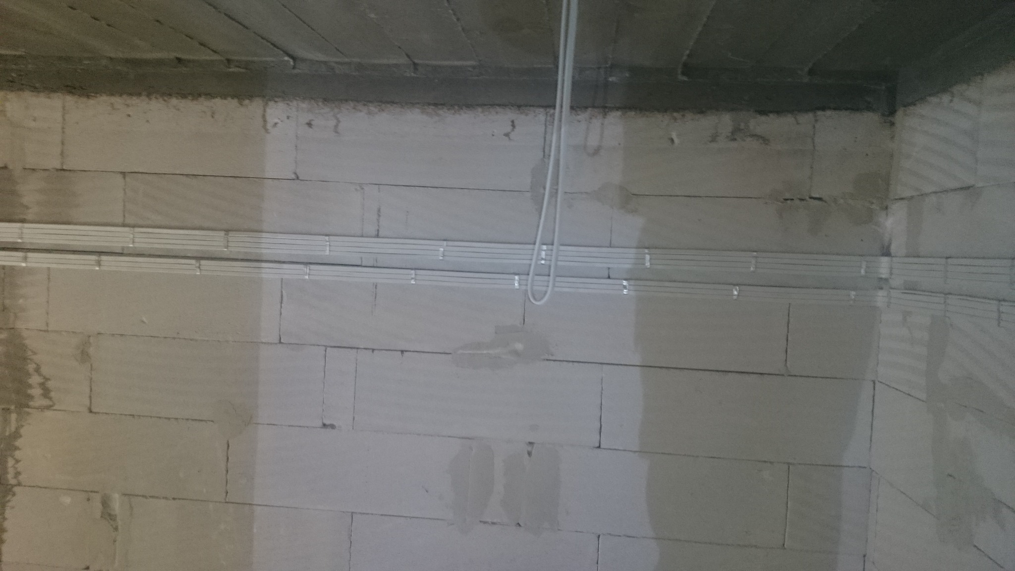 Surowy mur z betonu komórkowego z zamontowanymi metalowymi korytkami kablowymi i zwisającymi przewodami elektrycznymi w nowo budowanym pomieszczeniu.