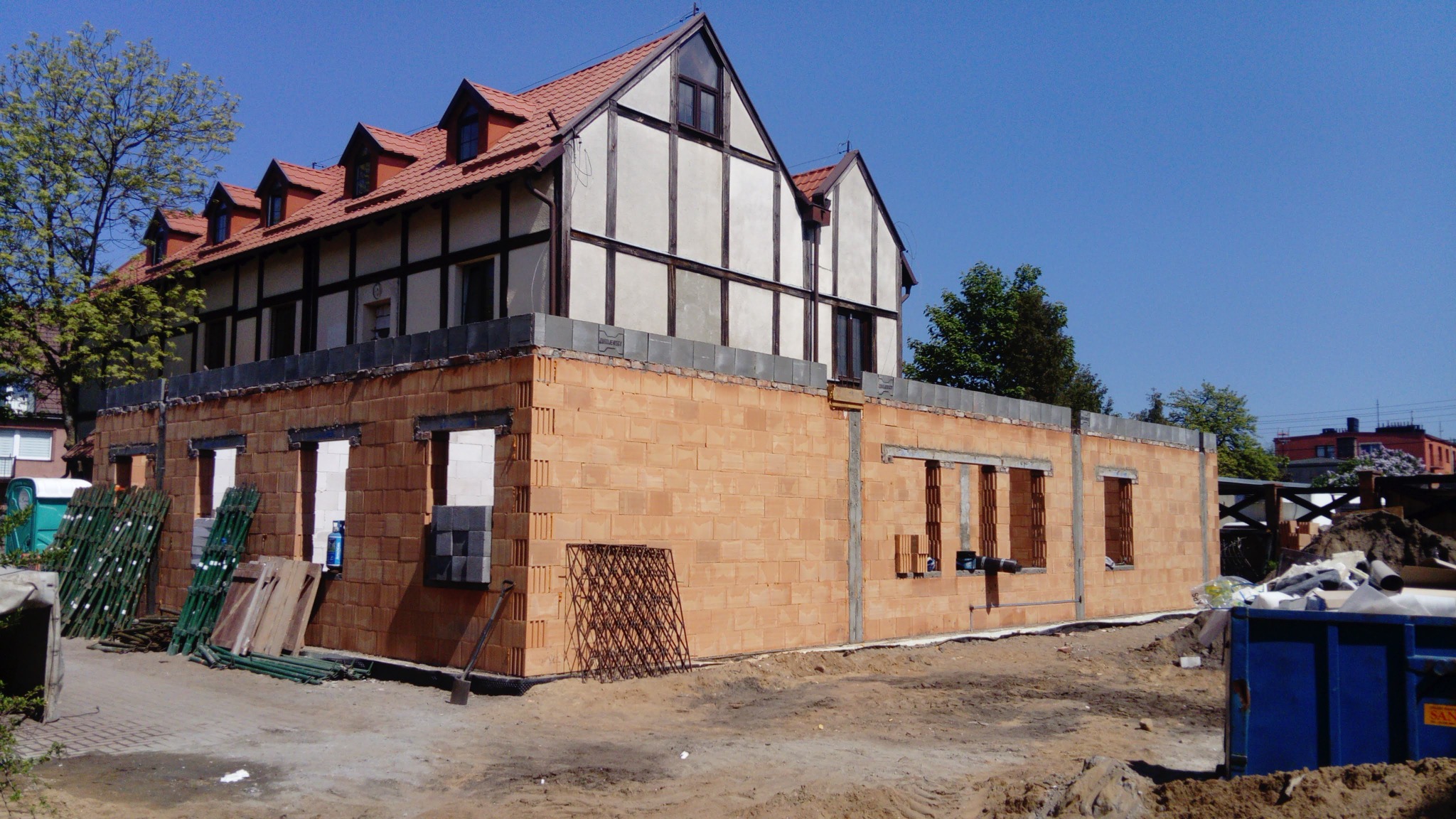 Budowa domu jednorodzinnego w stanie surowym otwartym: ściany z cegły ceramicznej, widoczne otwory okienne, w tle starsza część budynku z elementami muru pruskiego.