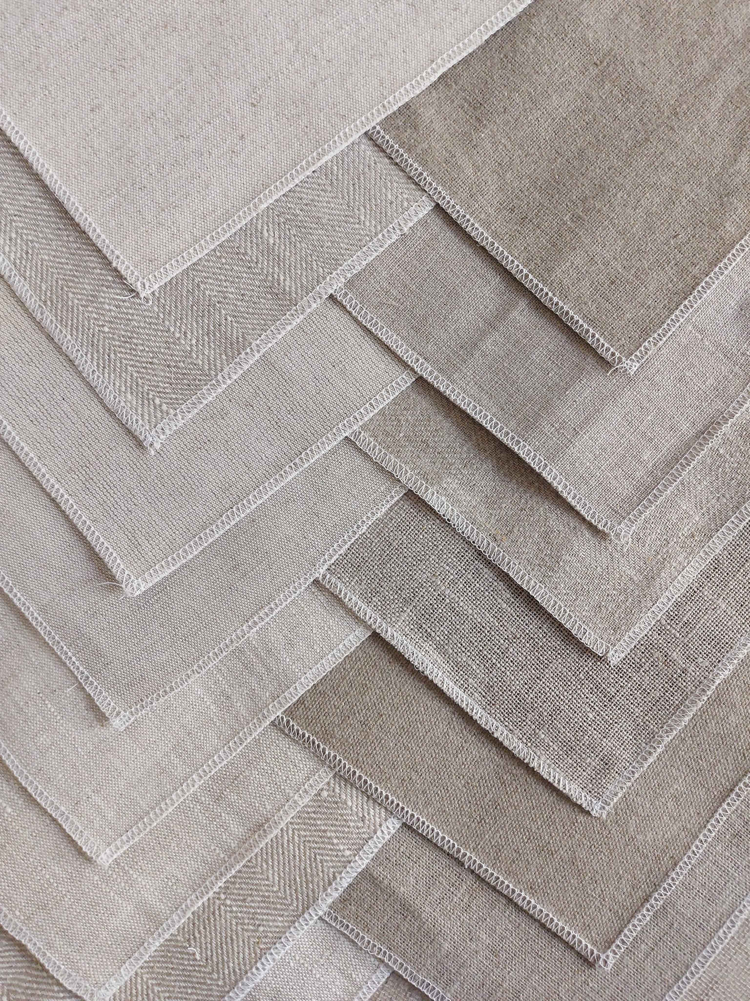 Ułożone pod kątem kwadratowe próbki tkanin w odcieniach beżu i szarości, z widocznym splotem i białym obszyciem.