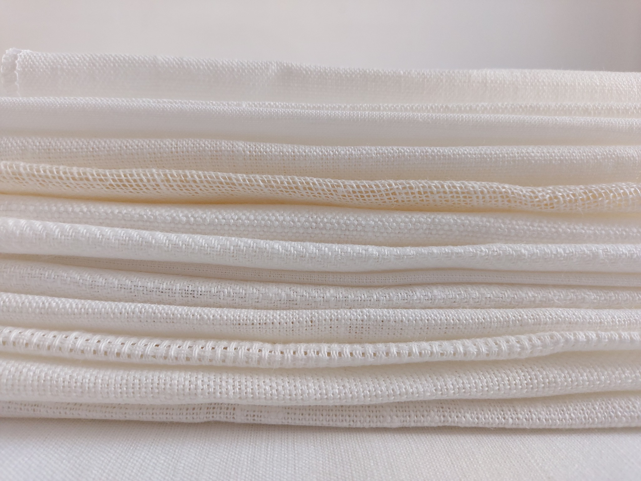 Stos białych, złożonych tkanin o różnych splotach, widoczne detale faktur i krawędzi