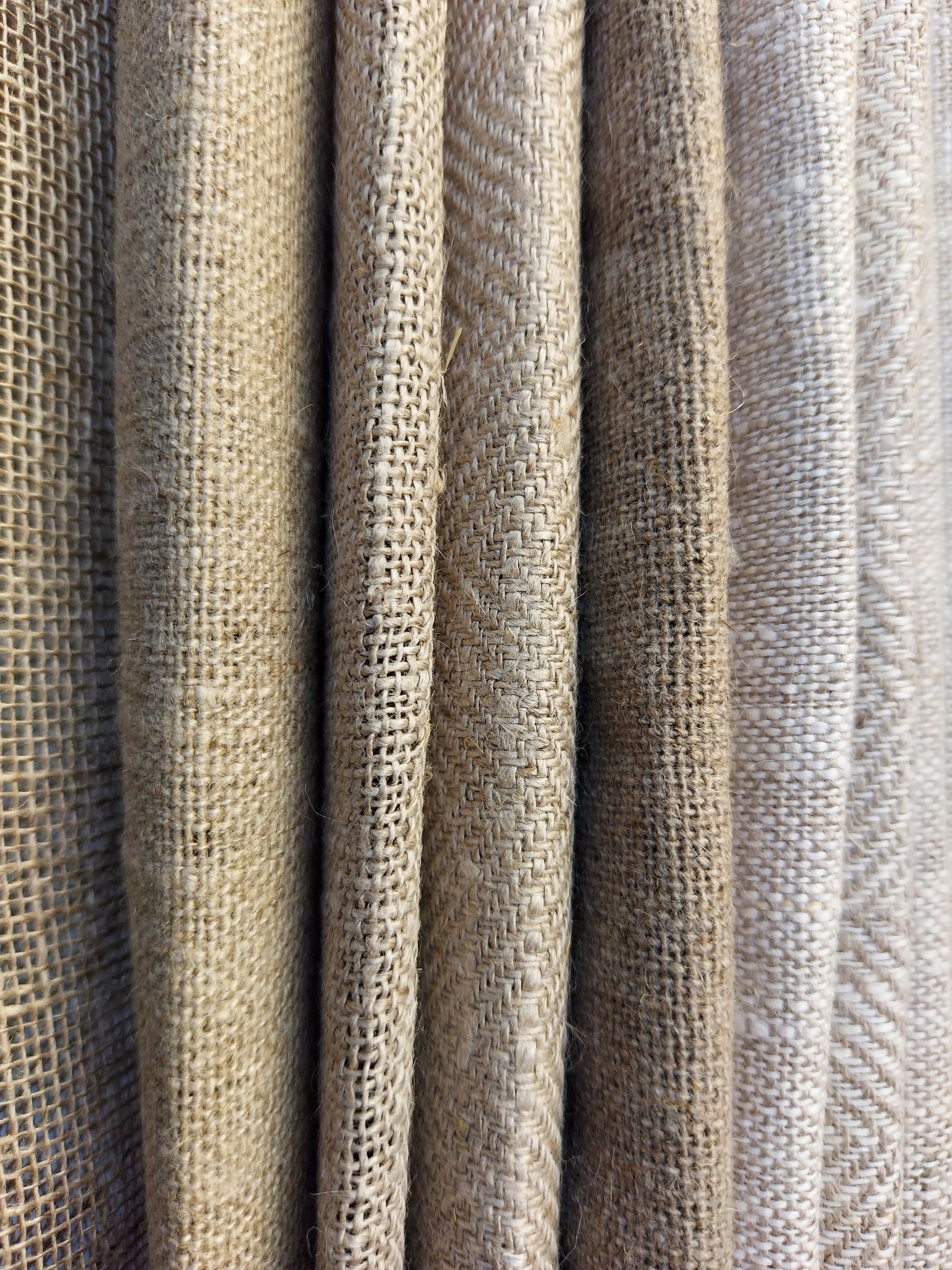 Detale beżowej, grubo tkanej tkaniny, układającej się w fałdy, z widoczną strukturą splotu.