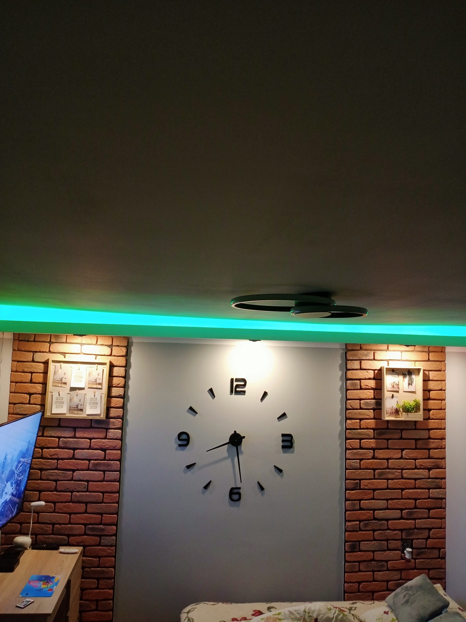 Ściana z cegły dekoracyjnej, podświetlony sufit z lampą i duży zegar ścienny w nowoczesnym wnętrzu.