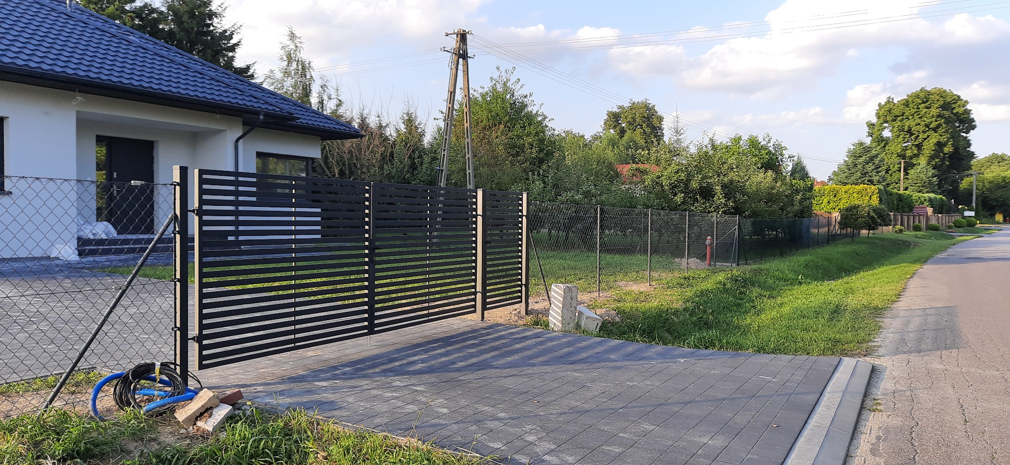 Nowoczesna, pozioma brama przesuwna z czarnych paneli w Bychawie, z widocznym fragmentem posesji i ogrodzeniem z siatki.