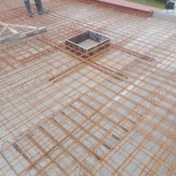 Zbrojenie płyty fundamentowej z otworem w Książu Wielkopolskim, przygotowane do zalania betonem, widoczne buty robotnika i częściowo samochód dostawczy w tle.