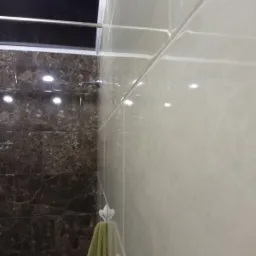 Wykończona łazienka z brązowymi i beżowymi błyszczącymi płytkami, widoczny reling i wieszak z ręcznikami, zbliżenie na fugi.