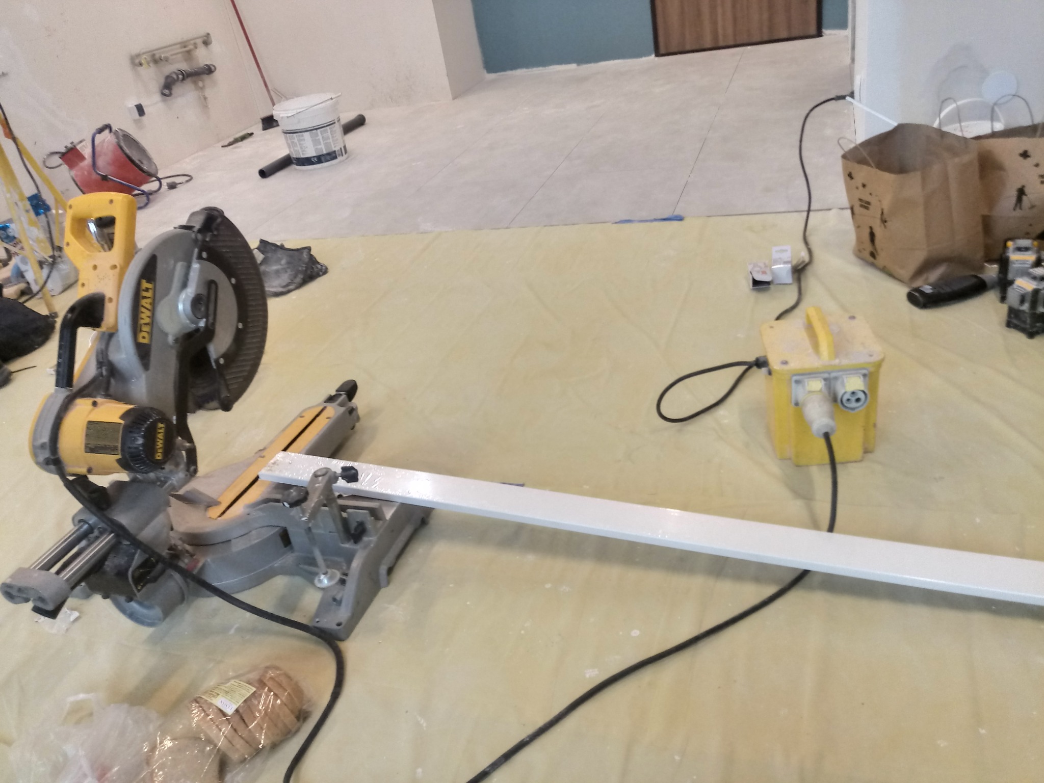 Ukośnica DeWalt ustawiona na folii ochronnej, przygotowana do cięcia białej listwy przypodłogowej w trakcie prac wykończeniowych w nowym wnętrzu.