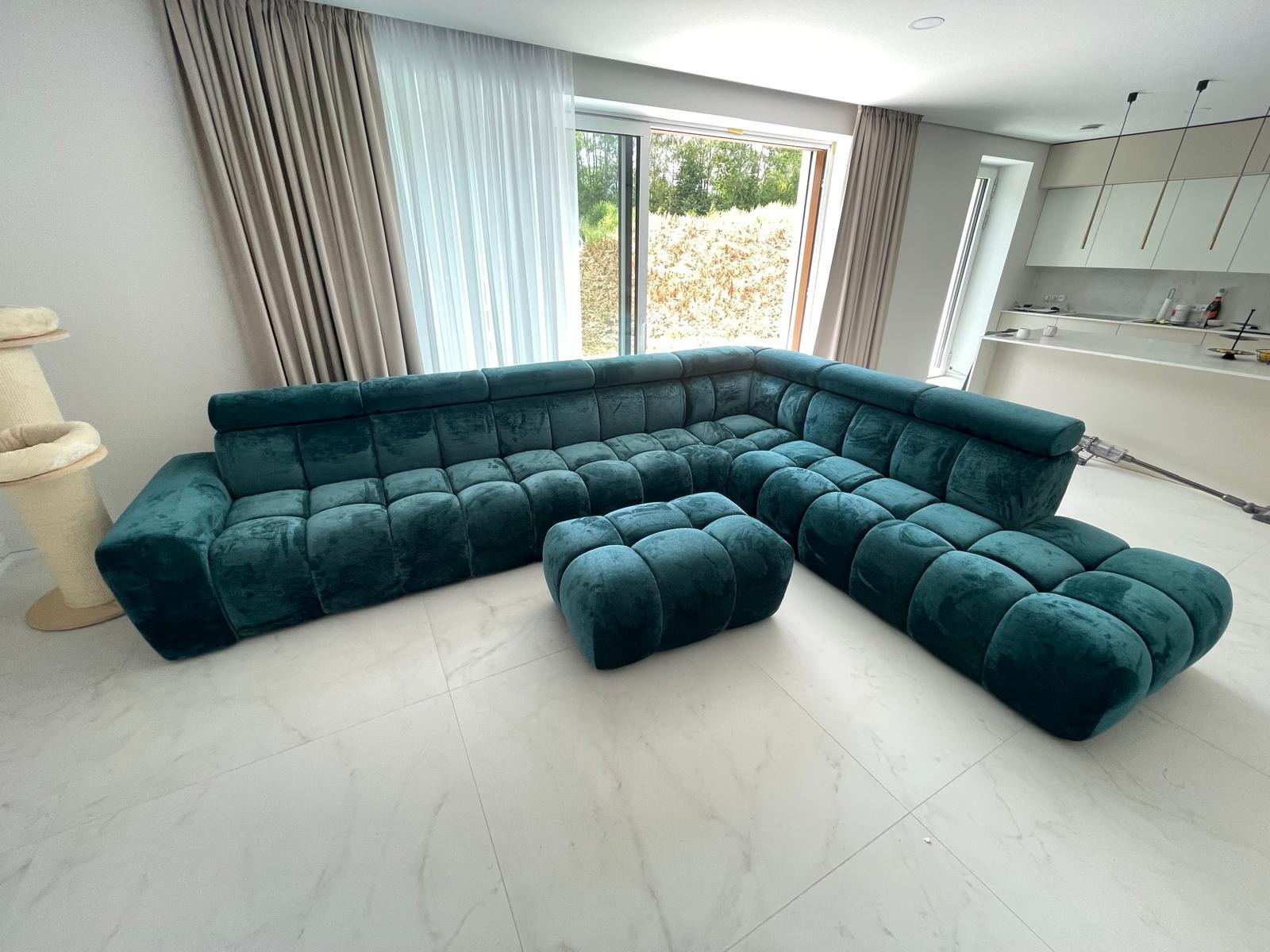 Turkusowy, modułowy narożnik z pufą w nowoczesnym salonie z marmurową podłogą i dużym oknem.