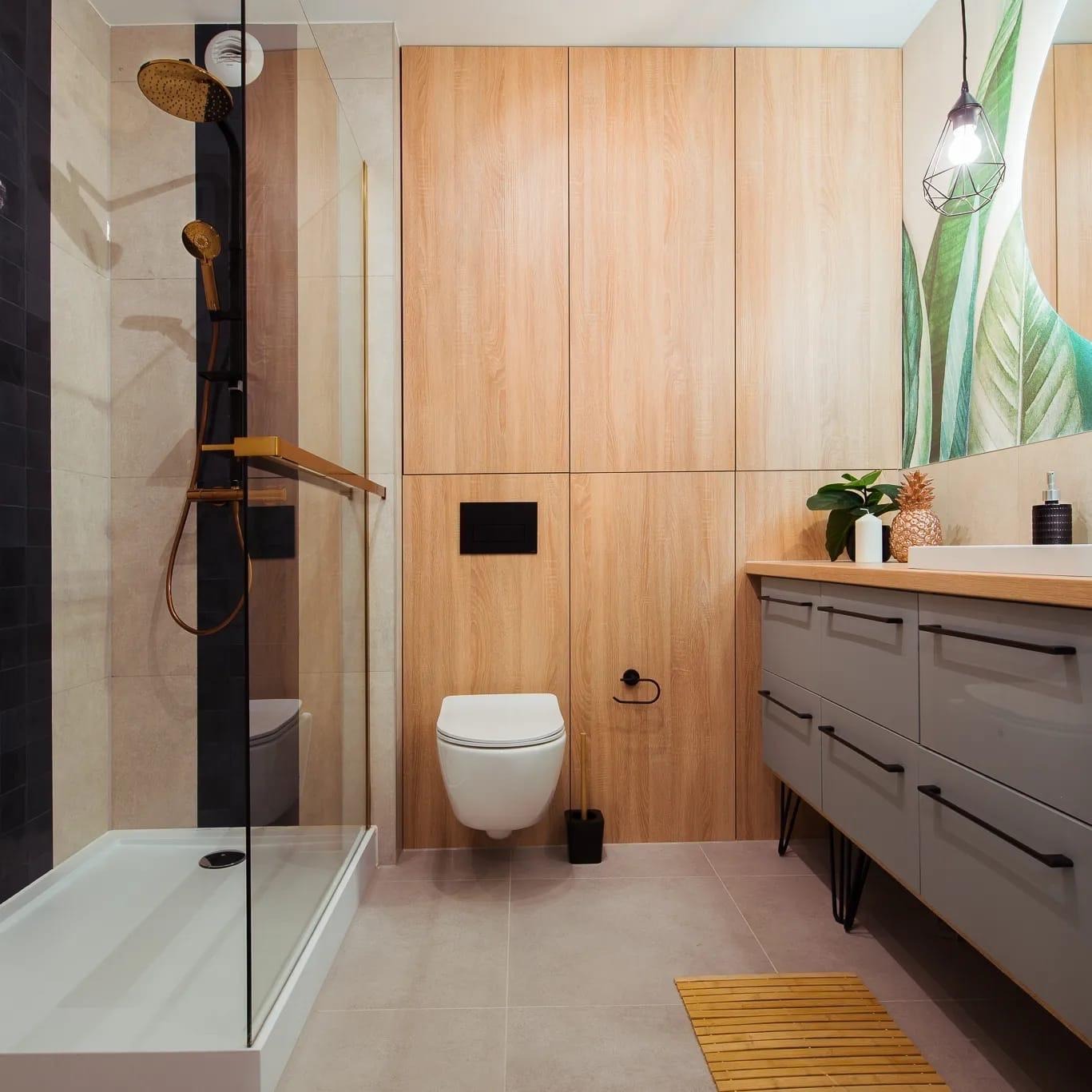 Nowoczesna łazienka z kabiną prysznicową typu walk-in, drewnianymi szafkami, szarą szafką pod umywalkę z czarnymi uchwytami i wiszącą toaletą.