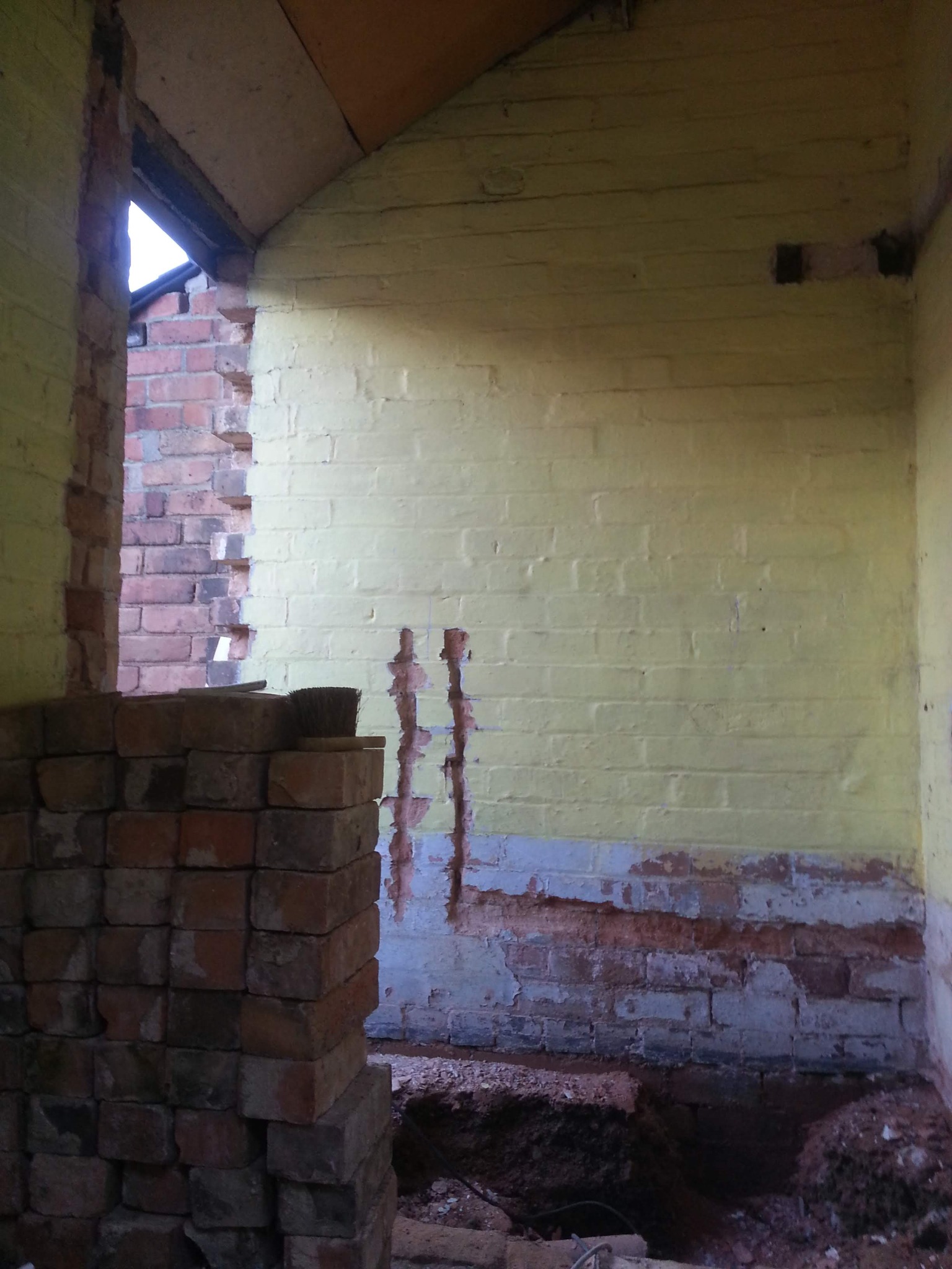 Wnętrze w trakcie remontu: sterta cegieł, fragment ściany z resztkami farby i odsłoniętą cegłą, widoczne ślady po instalacjach na ścianie, odsłonięta podłoga.