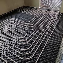 Układanie rur ogrzewania podłogowego na czarnej, perforowanej macie izolacyjnej, widok z góry, instalacja w trakcie montażu, jasne światło.