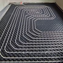 Rozłożone rury ogrzewania podłogowego na czarnej macie izolacyjnej z wypustkami, widok z góry, przed zalaniem wylewką.