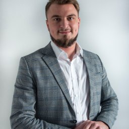 Loft Nieruchomości - Portret mężczyzny w szarej marynarce w kratę i białej koszuli, z rękami splecionymi na wysokości pasa, na jasnym tle.