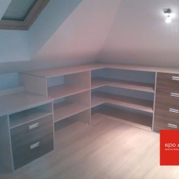 KĘDO Kędzior Dariusz - Zabudowa pod skosem na poddaszu z białymi półkami i szufladami w odcieniach brązu, widoczne okno dachowe i logo firmy meblowej w prawym dolnym rogu.