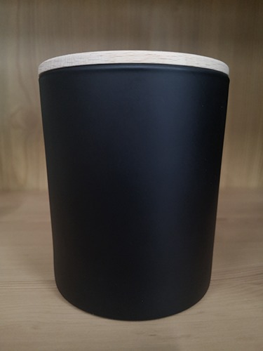 Matowy, czarny pojemnik cylindryczny z jasną, drewnianą pokrywką na jasnym blacie.