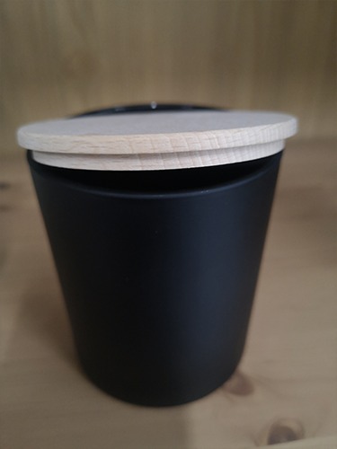 Czarny, matowy pojemnik z jasną, drewnianą pokrywką na drewnianym blacie, element kosza prezentowego.