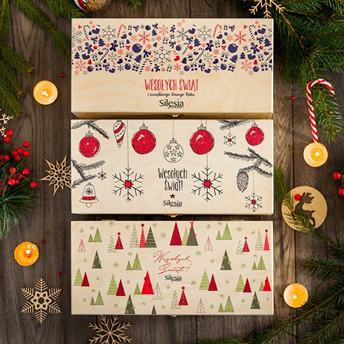 Trzy drewniane skrzynki z motywami świątecznymi: bombki, choinki, śnieżynki; dekoracje świąteczne, świece, gałązki choinki na drewnianym tle.