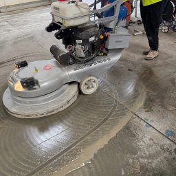 CleanQ - Mycie posadzki przemysłowej maszyną Levina B36 G-S. Widoczne ślady po czyszczeniu, operator w odblaskowej kamizelce. W tle wózek widłowy.