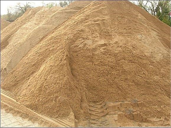 Duża pryzma piasku budowlanego z wyraźnymi śladami opon na zboczu, widok z dołu.