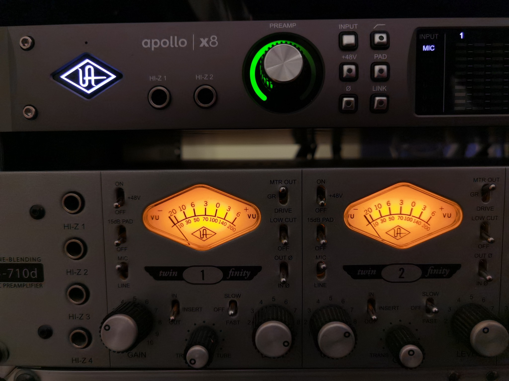 Sprzęt studyjny: interfejs audio Apollo x8 z podświetlonym logo i pokrętłem oraz przedwzmacniacz Universal Audio 710d z analogowymi wskaźnikami VU, przełącznikami i potencjometrami.
