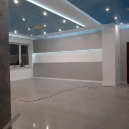 Wykończone wnętrze pokoju z sufitem napinanym z motywem chmur, gładkimi ścianami z poziomym pasem oświetlenia i błyszczącą podłogą.