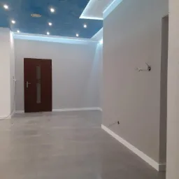 Pomalowane na szaro wnętrze z imitacją nieba na suficie, oświetleniem punktowym i listwami przypodłogowymi, widoczne wystające kable elektryczne.