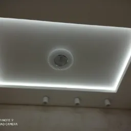 Podwieszany sufit z oświetleniem LED w kształcie prostokąta i dekoracyjną lampą centralną, uzupełniony trzema punktowymi reflektorami i kratką wentylacyjną, widok od dołu.