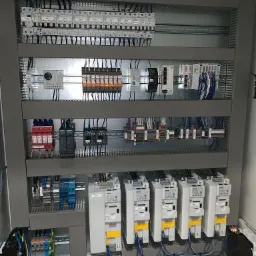 Wnętrze szafy sterowniczej z zamontowanymi modułami, bezpiecznikami i przekaźnikami, widoczne liczne przewody podłączone do poszczególnych elementów, szyna DIN na różnych poziomach szafy.