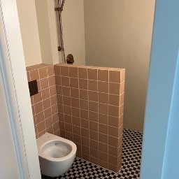 Fams bud - Nowoczesna łazienka z kabiną prysznicową oddzieloną niską ścianką z beżowych płytek. Umywalka podwieszana, podłoga w czarno-białą szachownicę, armatura w kolorze miedzi.