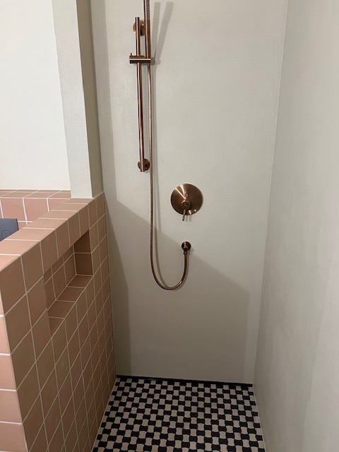 Wykończona kabina prysznicowa z miedzianą armaturą, czarno-białą mozaiką podłogową i różowymi płytkami. Minimalistyczny design z dbałością o detale.