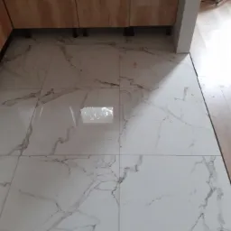 Białe, marmurkowe płytki podłogowe, widoczne nóżki szafek kuchennych z przodu.