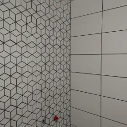 Ściana łazienki wyłożona białymi płytkami z czarnym wzorem geometrycznym tworzącym iluzję kostek 3D, sąsiadująca ze ścianą z prostokątnych, białych płytek z czarnymi fugami, widoczny czerwony zawór...