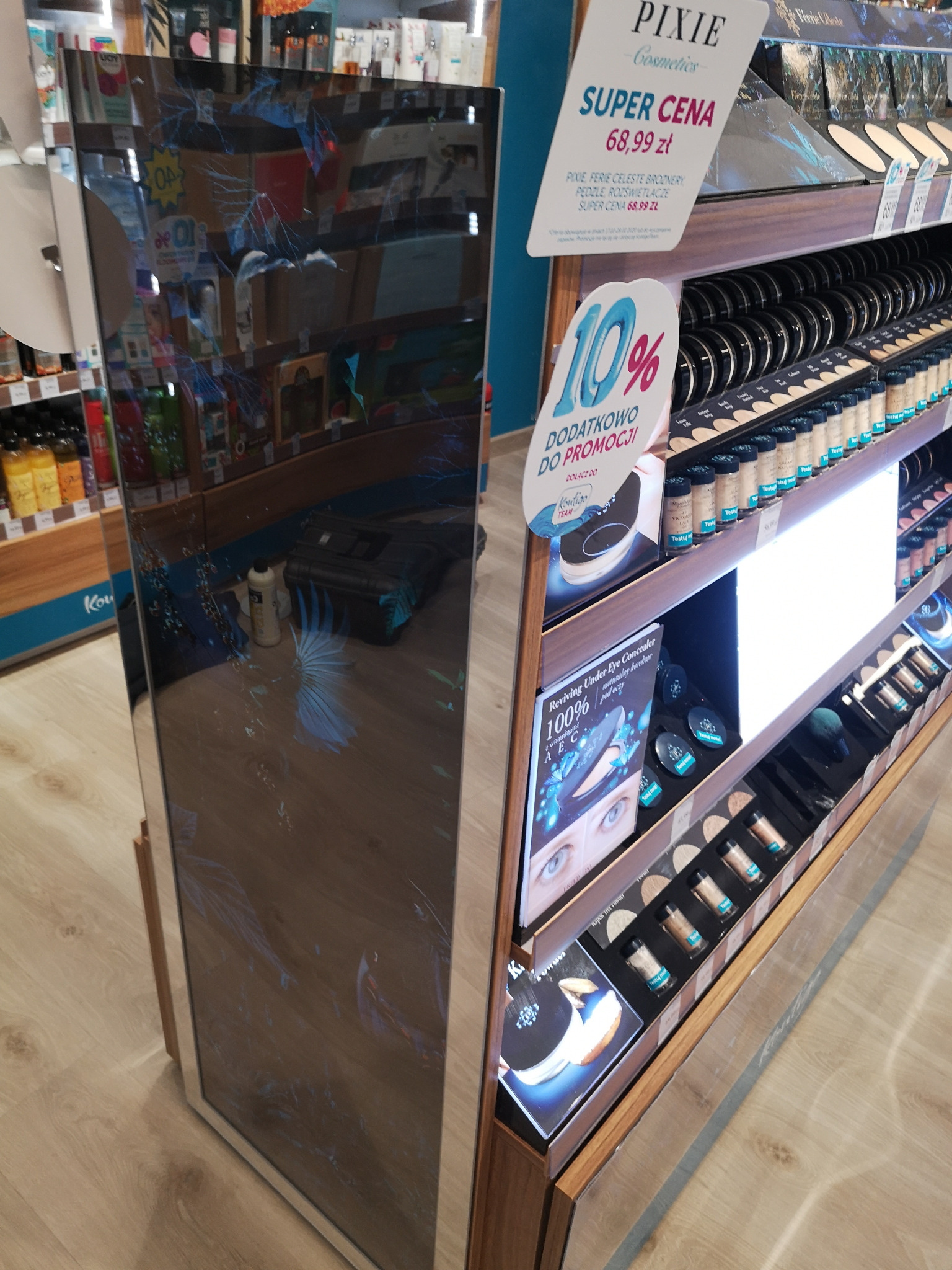 Duży, podświetlany panel reklamowy w sklepie z kosmetykami, prezentujący produkty do makijażu, z widocznymi refleksami i odbiciami otoczenia.
