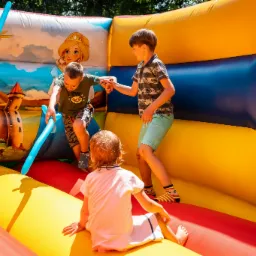 Kilka rozbawionych dzieci bawi się w dmuchanym zamku z namalowaną scenerią zamku i postacią księżniczki, trzymając w rękach balonowe miecze.