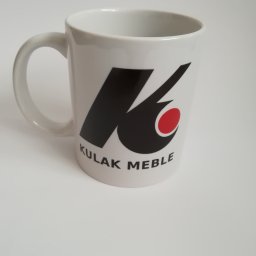 Seleo Druk - Biały kubek z czarno-czerwonym logo firmy Kulak Meble na jednolitym, jasnym tle.