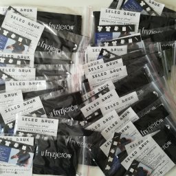 Seleo Druk - Stos pakowanych maseczek i ulotek reklamowych z nadrukiem logo 'SELED DRUK' i informacją o nadrukach na koszulkach, body dziecięcych, kubkach i torbach, przeznaczonych dla fryzjerów.