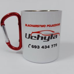 Seleo Druk - Biały kubek z karabińczykiem jako uchwyt, nadrukiem firmy blacharskiej 'Uchyla' oraz numerem telefonu, na białym tle.