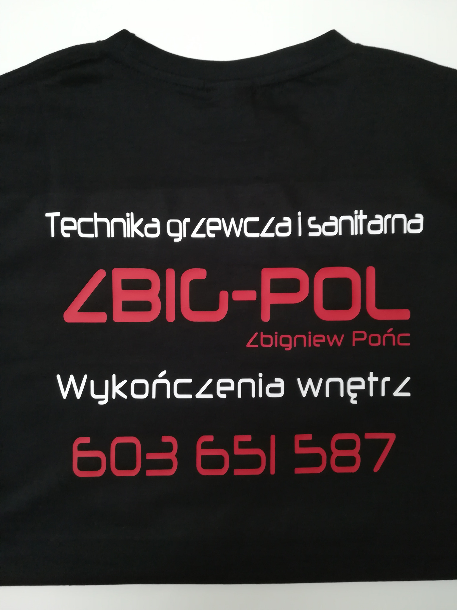 Czarna koszulka z białym i czerwonym nadrukiem prezentująca firmę z Zabłocia: 'Technika grzewcza i sanitarna ZBIC-POL Zbigniew Pońc Wykończenia wnętrz 603 651 587'.