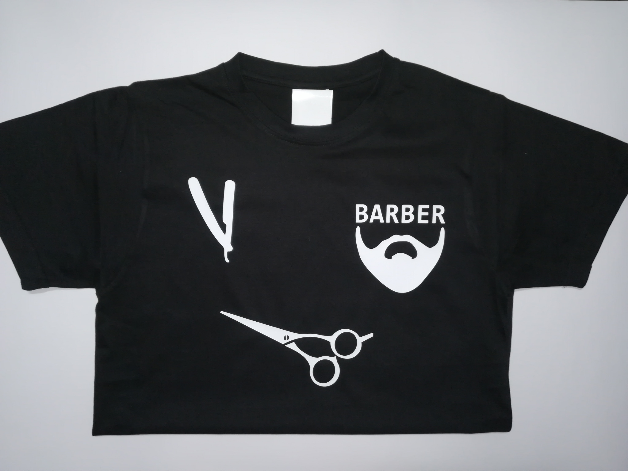 Czarna koszulka z białym nadrukiem fryzjerskim: brzytwa, nożyczki i broda z napisem 'BARBER'.