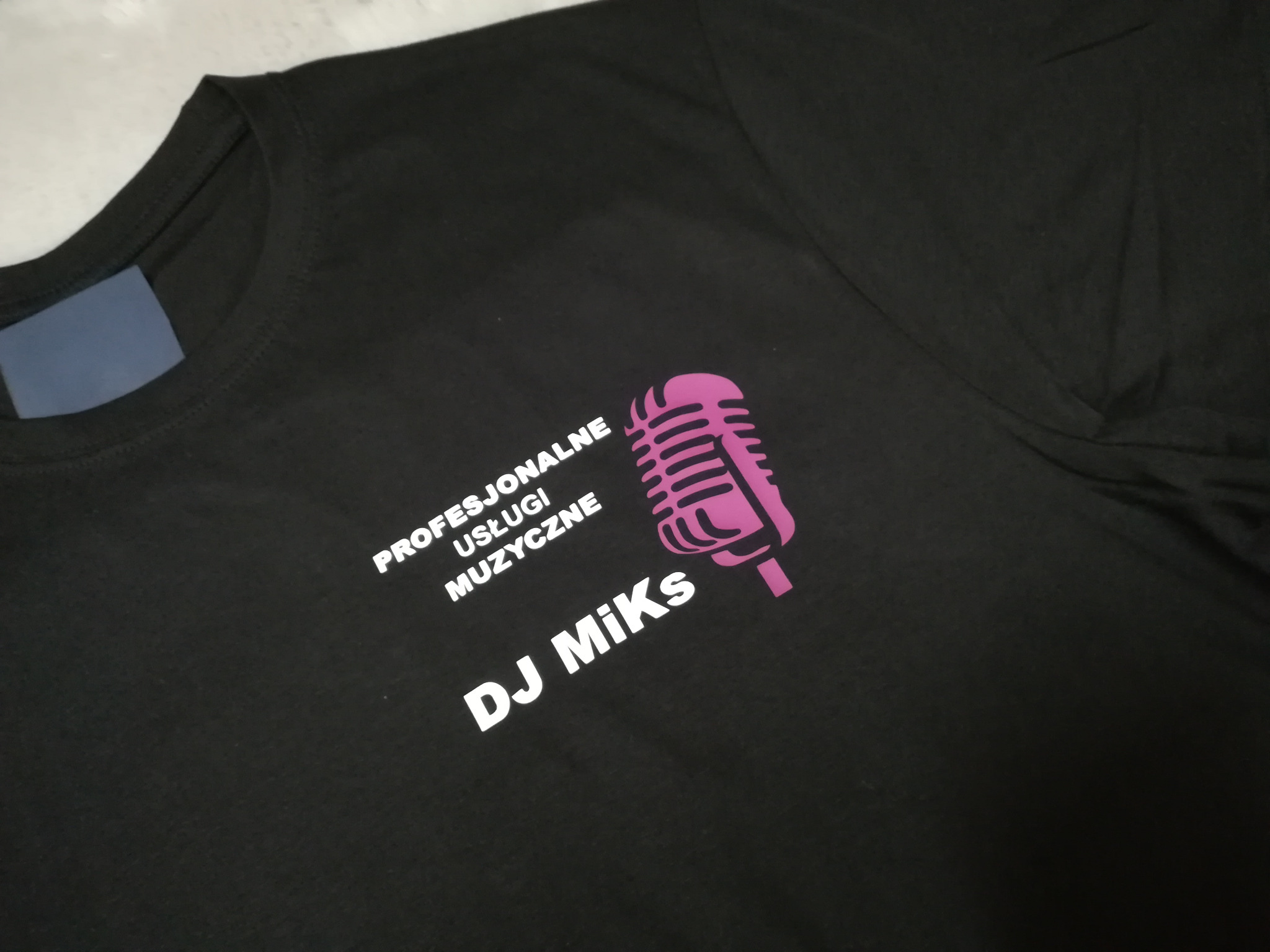 Czarna koszulka z nadrukiem 'Profesjonalne Usługi Muzyczne DJ Miks' oraz grafiki mikrofonu w kolorze fuksji.