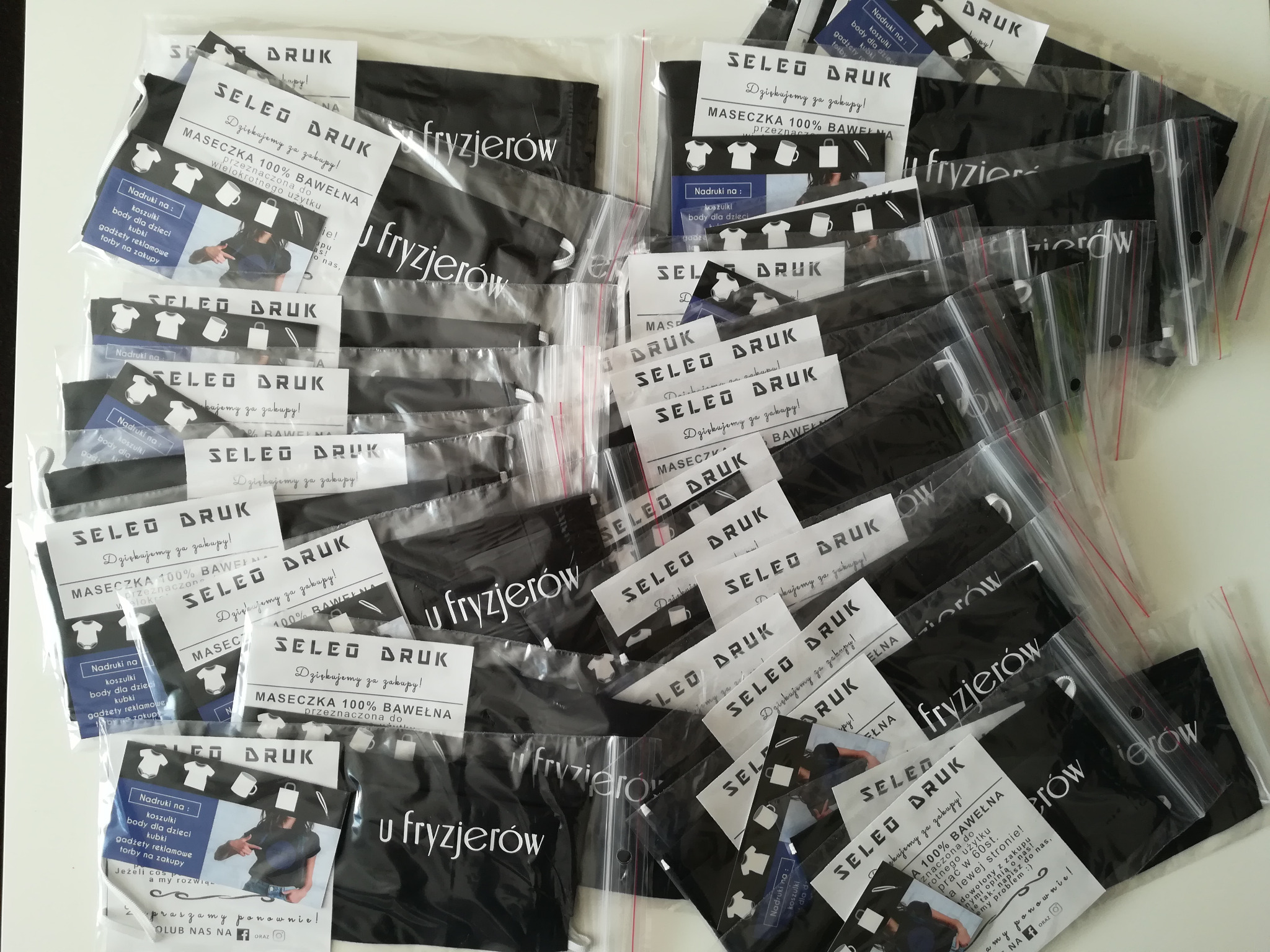 Stos pakowanych maseczek i ulotek reklamowych z nadrukiem logo 'SELED DRUK' i informacją o nadrukach na koszulkach, body dziecięcych, kubkach i torbach, przeznaczonych dla fryzjerów.