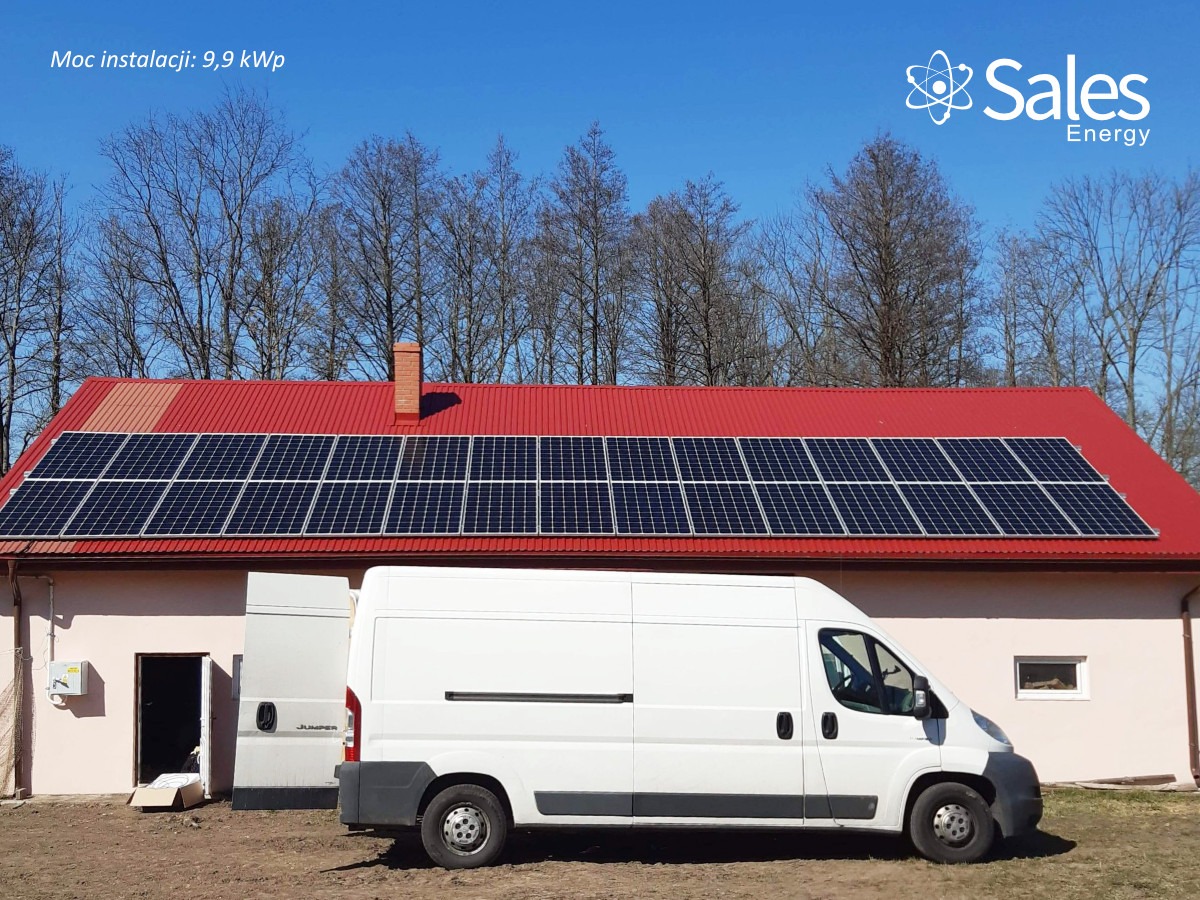 Instalacja paneli słonecznych na czerwonym dachu budynku jednorodzinnego o mocy 9.9 kWp, z zaparkowanym białym vanem dostawczym firmy Sales Energy obok budynku.