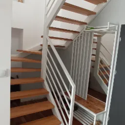 Nowoczesne schody drewniane z białymi metalowymi barierkami i zabudowaną szafką na buty z lustrem, parkiet w odcieniach brązu.