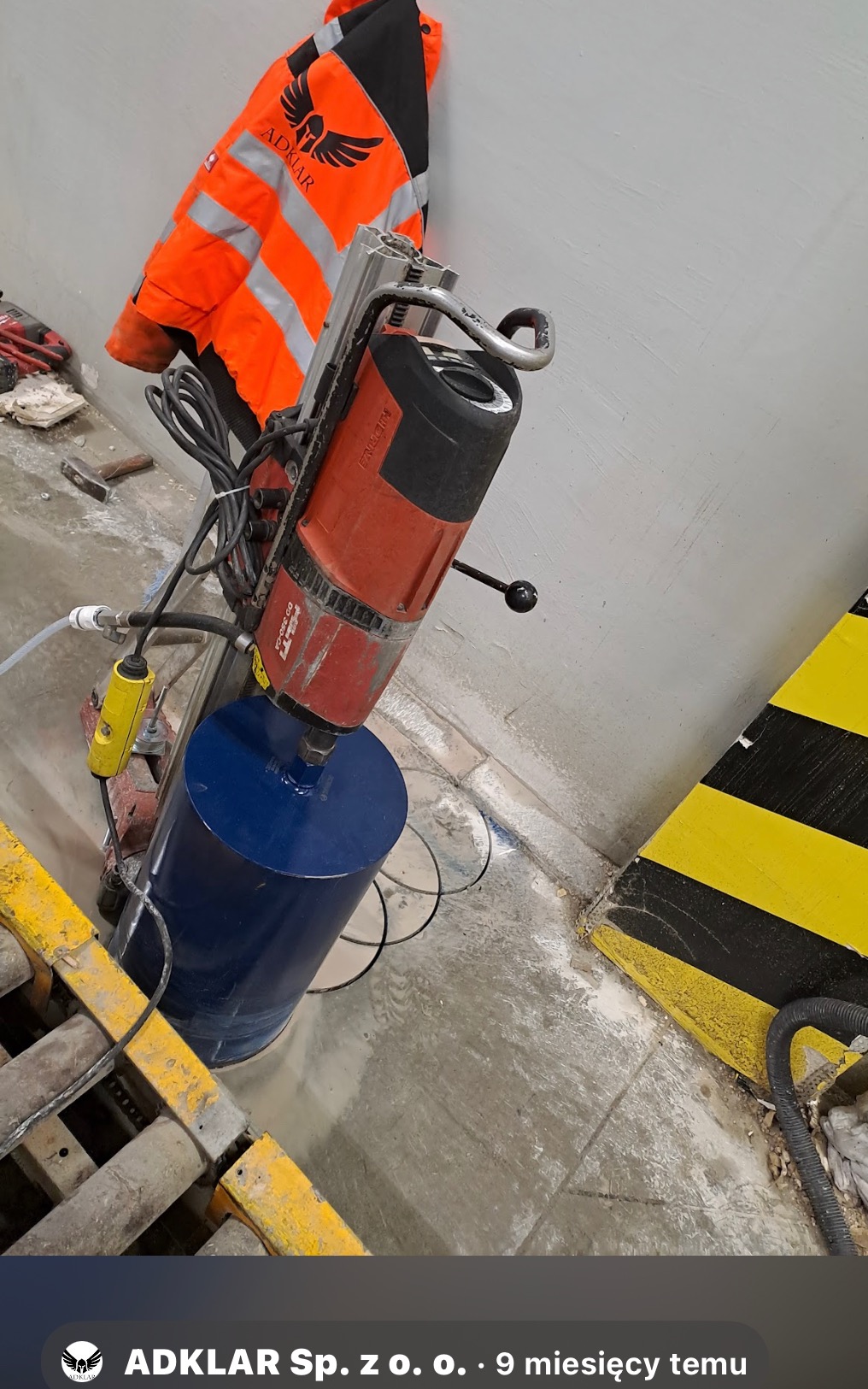 Wiertnica rdzeniowa Hilti DD 350-CA z niebieską koronką diamentową podczas wiercenia w szarym betonie, obok leży pomarańczowa kurtka robocza z logo firmy ADKLAR.